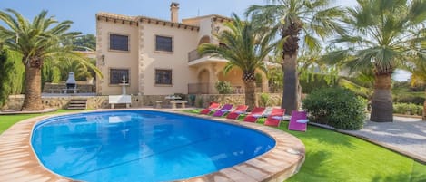 Una piscina de borde curvo, rodeada de césped cuidado y palmeras.