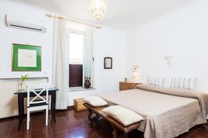 A bedroom with a bed, a desk, a chair, a window with curtains, and a radiator.
