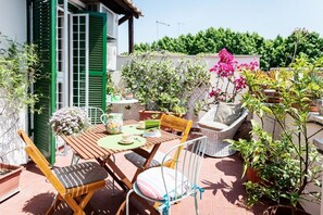 A patio with a wooden table, two chairs, a wicker sofa, and potted plants.