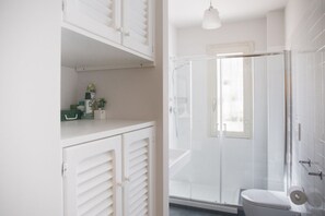 A bathroom with a glass shower enclosure, a toilet, and a cabinet with storage space.