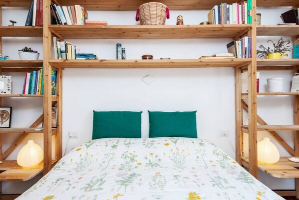 A bedroom with a bed, two green pillows, and wooden bookshelves filled with books and decorative items.