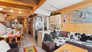 En hyggelig stue med træloft, en sofa med mønstrede puder, et sofabord og et spiseområde med et bord dækket til to personer.