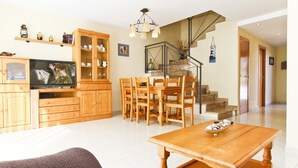Una sala de estar moderna con una mesa de comedor de madera, un sofá y un televisor. Una escalera conduce a otro nivel.