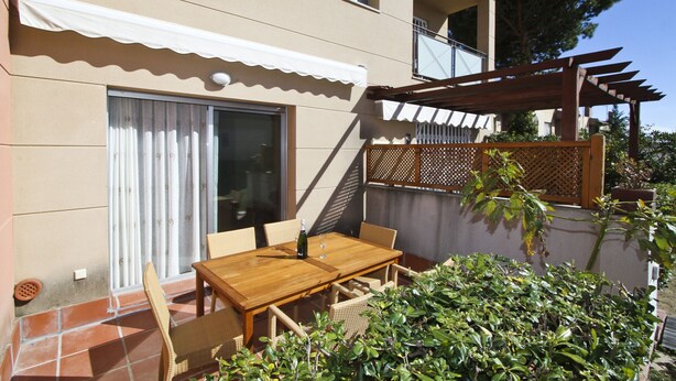 Un patio con mesa y sillas de madera, una botella de vino y una copa.