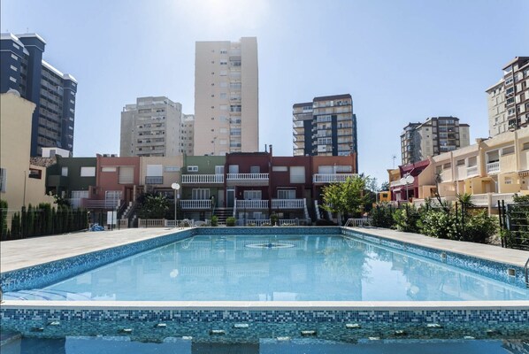 A swimming pool with a tiled edge, surrounded by multi-story residential buildings.