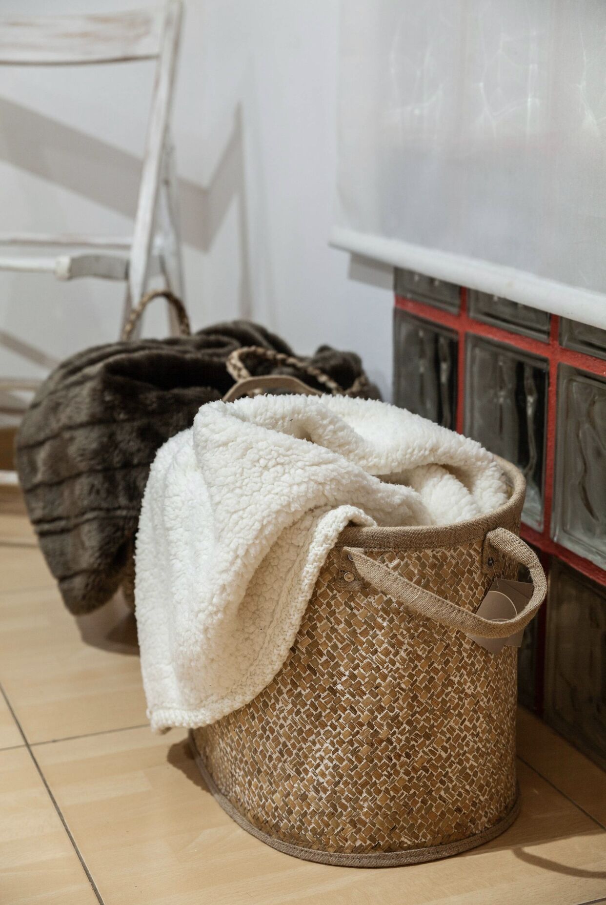 Ein Zimmer mit einem weißen Stuhl, einem gewebten Korb mit weißem Stoff und einer dunklen Tasche.