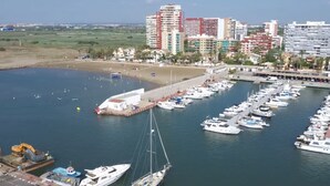 Un port de plaisance où sont amarrés de nombreux bateaux, une plage de sable et un paysage urbain avec des immeubles de grande hauteur en arrière-plan.