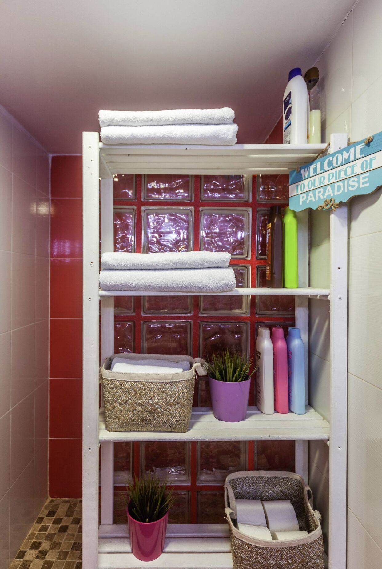 Een badkamer met een witte handdoekhouder, planken met toiletartikelen en een welkomstbord.