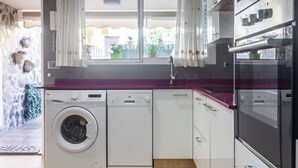 Une cuisine moderne équipée d’un lave-linge, d’un four encastré et offrant une vue sur l’extérieur.