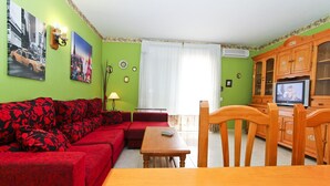 A living room with a red sofa, a wooden dining table, and a TV on a wooden cabinet. - MAR PINEDA Apartment (La Pineda)