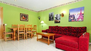 A living room with a red sofa, wooden chairs, a dining table, and green walls. - MAR PINEDA Apartment (La Pineda)