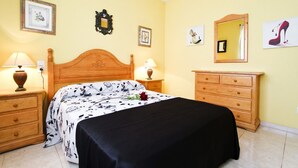 A bedroom with a wooden bed, two bedside tables with lamps, a dresser, and wall-mounted artwork. - MAR PINEDA Apartment (La Pineda)