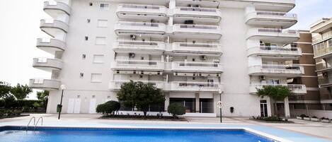 A multi-story residential building with balconies, a swimming pool, and a landscaped area with trees.