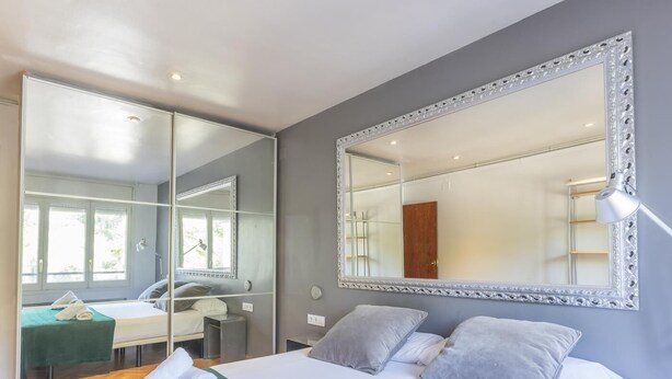 A modern hotel room with a large bed, a sitting area with a desk, and a large mirror. - My Space Barcelona apartment very close to Teknon Medical Center (Barcelona)