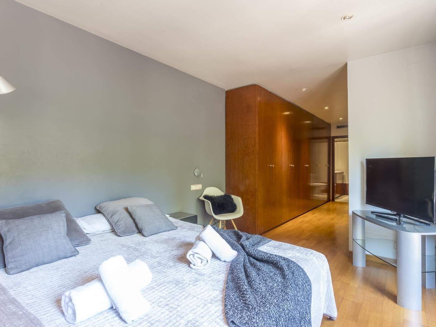 A modern hotel room with a large bed, a flat-screen TV, and a wooden wardrobe.