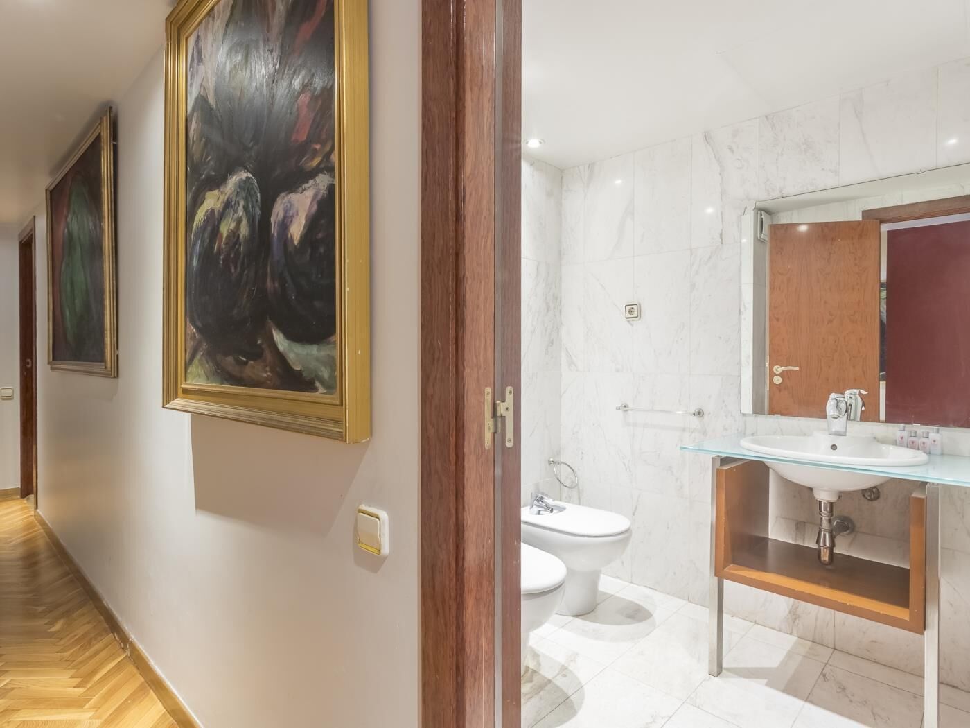 Un baño moderno con lavamanos de cristal, paredes de mármol y puerta de madera.