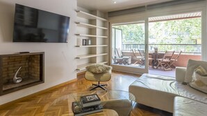 A modern living room with a flat-screen TV, a fireplace, a glass coffee table, a sofa, and a balcony with outdoor furniture. - My Space Barcelona apartment very close to Teknon Medical Center (Barcelona)