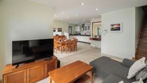 Ein modernes Wohnzimmer mit Flachbildfernseher, Holzmöbeln, einem grauen Sofa und einer Treppe, die nach oben führt.