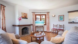Uma sala de estar com lareira, televisão e vista para o mar através de uma janela.