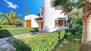 Um edifício branco com persianas de madeira, rodeado por vegetação exuberante e palmeiras.