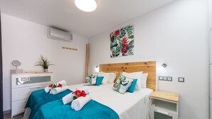 Une chambre d’hôtel avec deux lits, une tête de lit en bois, une table de chevet, une petite table d’appoint, un climatiseur mural, une œuvre d’art décorative accrochée au mur et une petite plante en pot.
