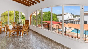 Ein sonnendurchfluteter Raum mit Esstisch und Stühlen, großen Bogenfenstern und Blick auf einen Pool und eine Außenanlage.