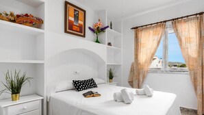 Ein Hotelzimmer mit einem Bett, einem Nachttisch, einem Regal mit Dekoration und einem Fenster mit Vorhängen.