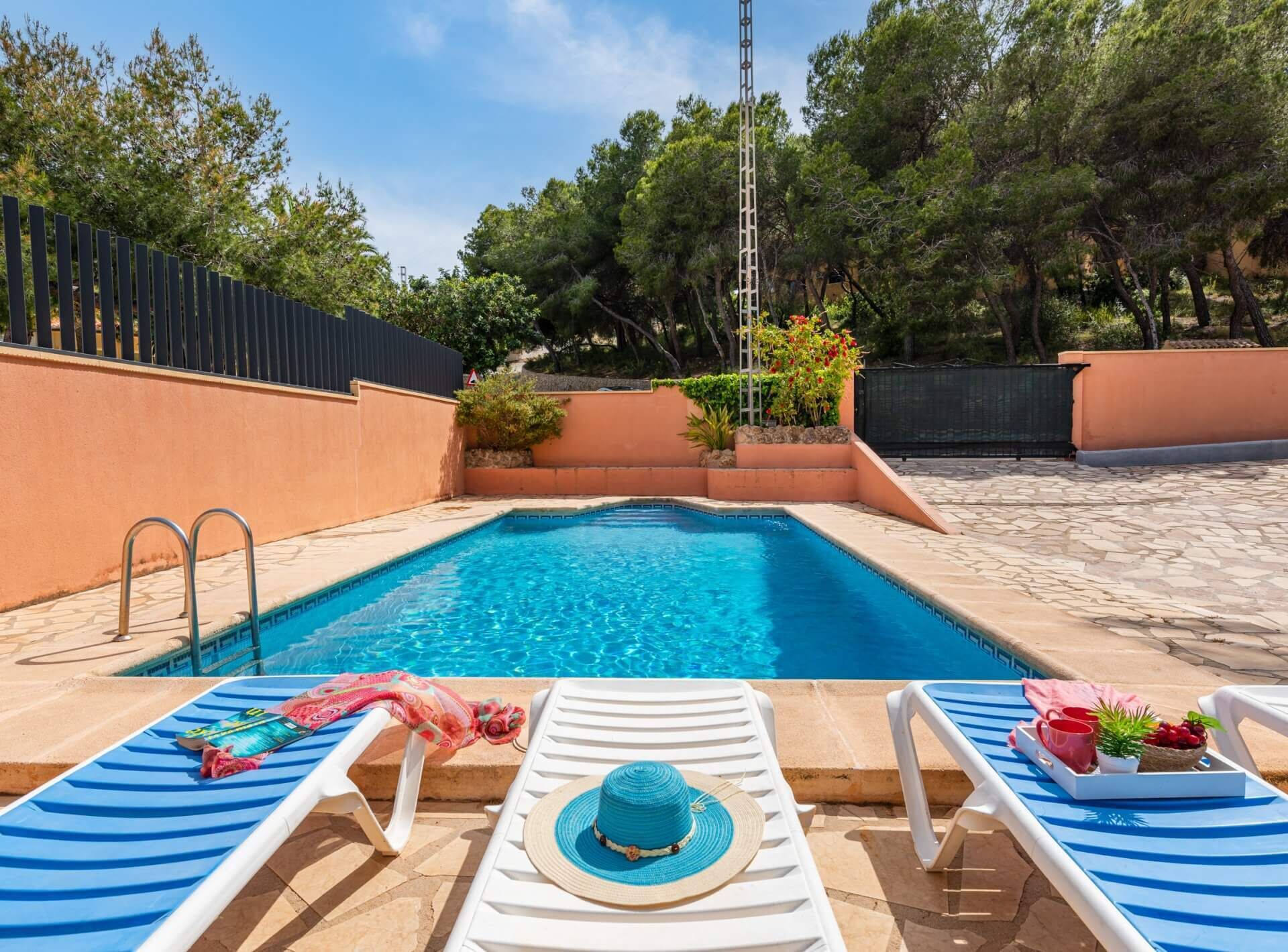Una piscina con sillas de descanso y una escalera, rodeada de árboles y una valla.