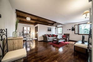 A spacious living area with a wooden ceiling, a dining table with chairs, a sofa set, and a television on a stand. - Mansarda Magritte (Venice)