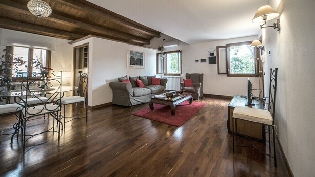 A living room with a wooden ceiling, a sofa set, a coffee table, and a dining area with a table and chairs. - Mansarda Magritte (Venice)