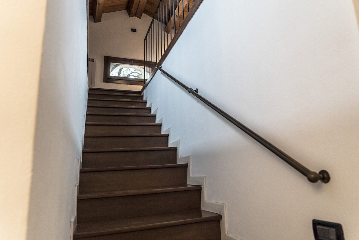 A staircase with wooden steps and a metal handrail, leading to a landing with a window.