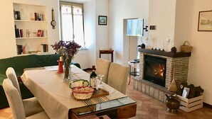 Ein gemütliches Wohnzimmer mit Kamin, einem Esstisch mit Blumenvase und einem Bücherregal voller Bücher und Dekorationsgegenstände.