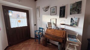 Ein Zimmer mit einer Holztür, einem blauen Stuhl, einer Holzkommode und einem weißen Stuhl. Mehrere gerahmte Bilder hängen an der Wand.