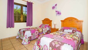 A bedroom with two beds, purple curtains, a wooden headboard, a nightstand, and a window with curtains.