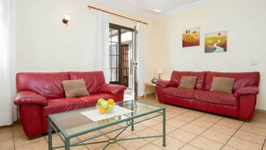 A living room with two red leather sofas, a glass coffee table with fruit, and a door leading outside.