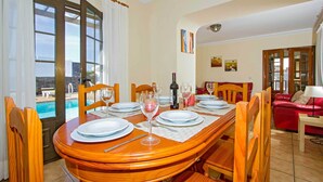 A dining area with a wooden table set for six, a pool view, and a red sofa in the background.