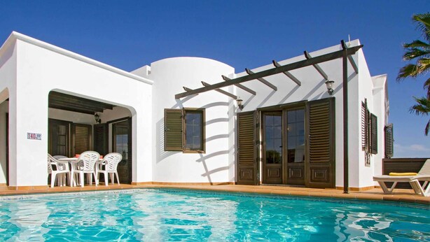 A white building with a pool, outdoor seating, and a pergola.