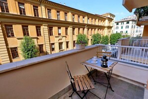 Un balcon avec une table et des chaises, un pot de fleurs et une vue sur un immeuble doté de nombreuses fenêtres.