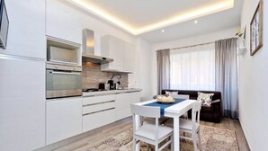 A modern kitchen with built-in appliances, a dining area with a table and chairs, and a living area with a sofa and curtains.