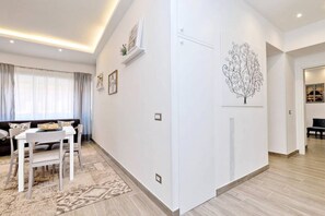 A modern living room with a dining area, a white sofa, a dining table, and a patterned rug.