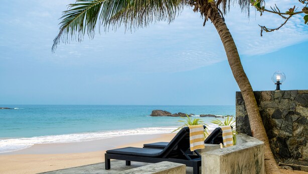 Eine Strandlounge mit Blick auf den Ozean, einer Palme und einer Steinmauer.