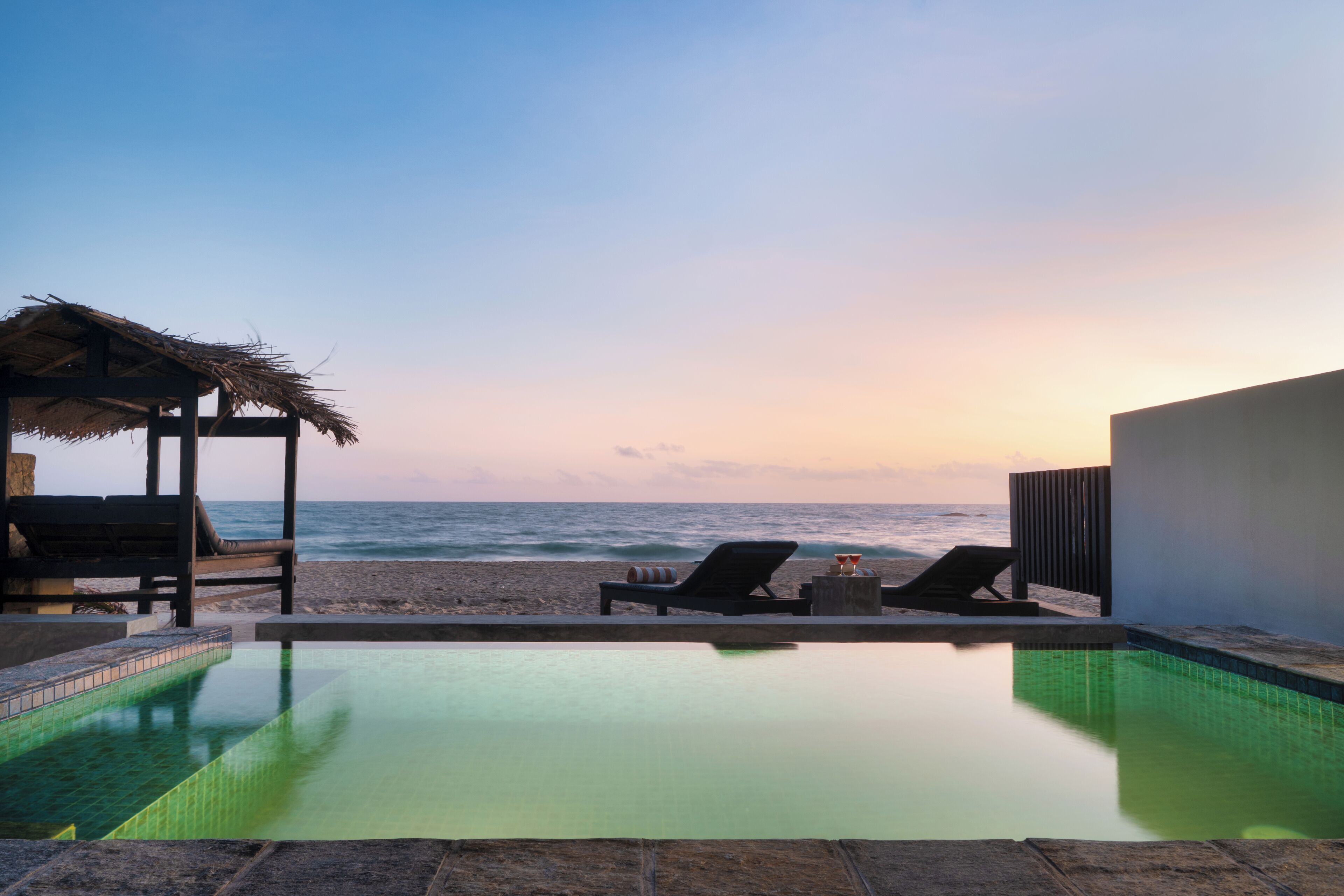 A poolside view with lounge chairs, a small pool, and a beach in the background.