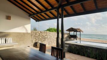 An outdoor seating area with a table and chairs, a stone wall, and a view of the beach and ocean.