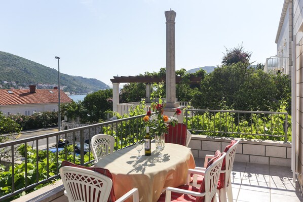 A balcony with a table set for two, a pergola, and a view of a hillside.
