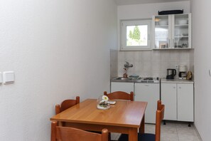 A small kitchen with a dining table and chairs, a window above the sink, and a cabinet with dishes.