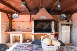 Una cocina rústica al aire libre con horno de ladrillo, un lavamanos y una mesa con una cesta de pan.