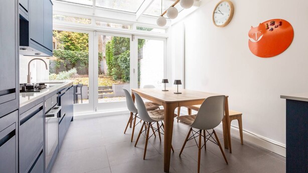 A modern kitchen with a dining area, large windows, and a view of the garden.
