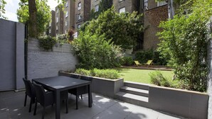 An outdoor patio with a table and chairs, surrounded by a brick wall and greenery.