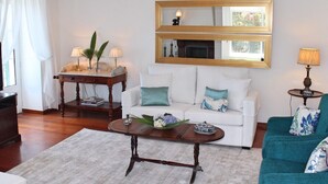 Ein Wohnzimmer mit einem weißen Sofa, einem türkisblauen Sessel, einem Couchtisch, einem Fernseher, einem Kamin und einem Spiegel.