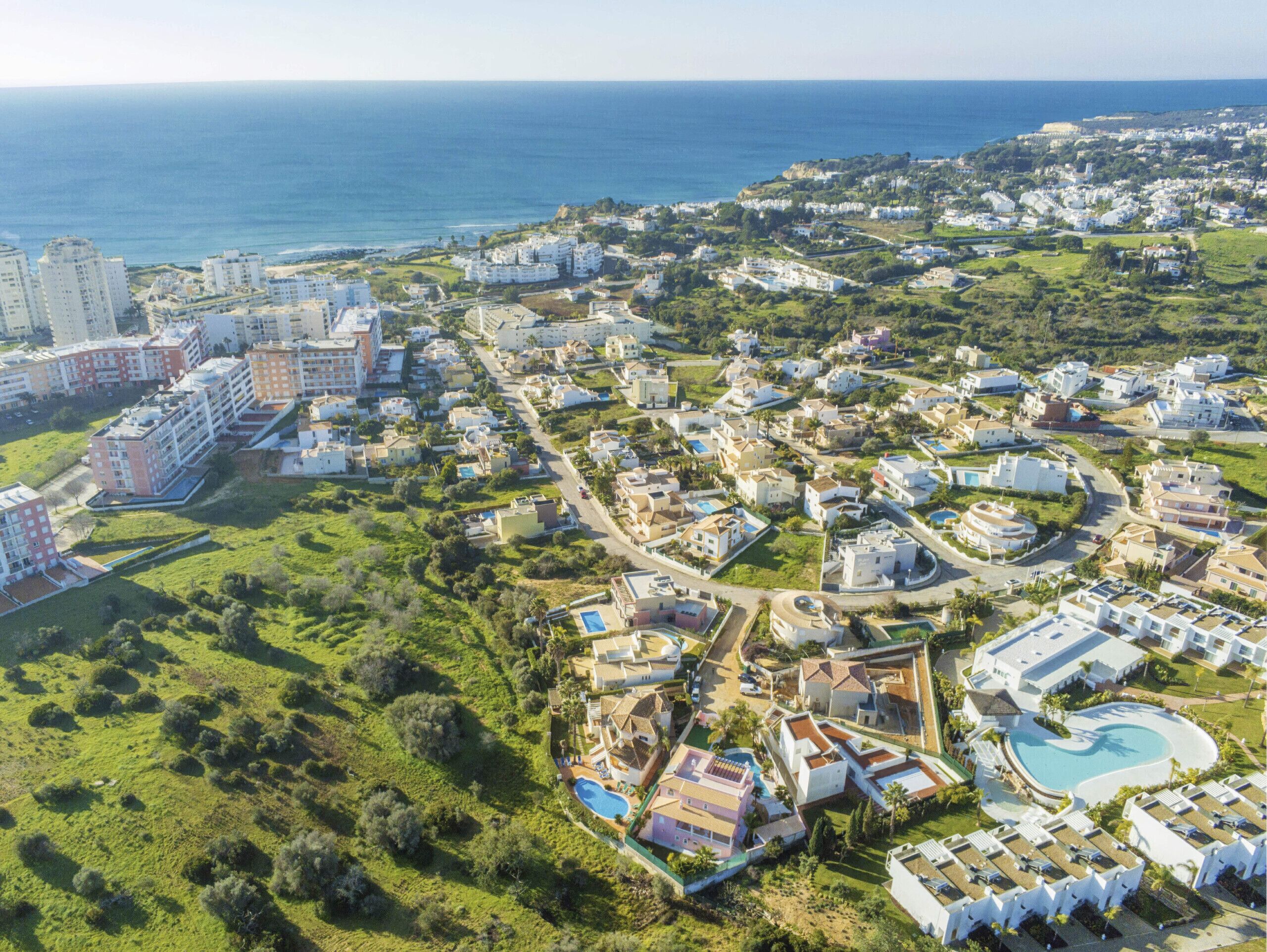 An aerial view of a coastal resort with multiple buildings, a swimming pool, and a view of the sea.